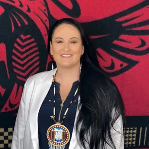 Smiling woman with long black hair and beaded jewelry.